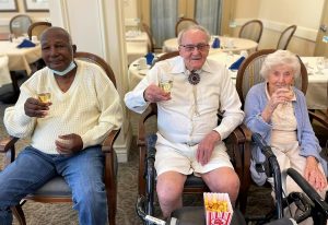 Three older adults sitting, multicultural, cheers, eating popcorn